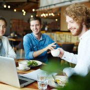 Three friends enjoying coffee and salad while using a laptop.