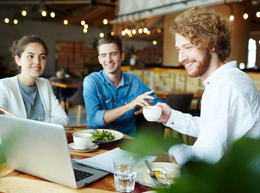 Three friends enjoying coffee and salad while using a laptop.