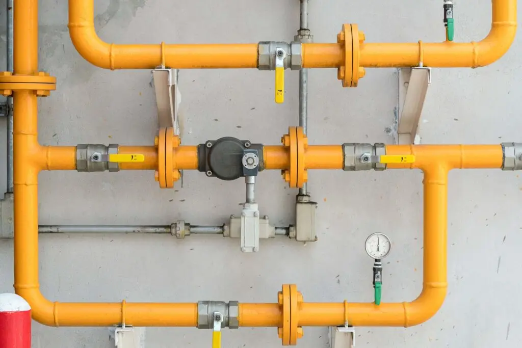 Orange industrial pipes with valves and gauge.